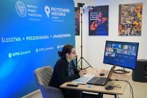 Zdjęcie prezentuje dr. Zofię Fenrych, która za biurka na tle turkusowej ścianki reklamowej prowadzi zajęcia dla nauczycieli. Przed nią stoi monitor na którym prowadzona jest transmisja dla nauczycieli