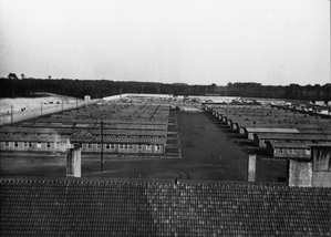 Widok obozu barakowego z rzędami baraków 1 i 2 obozu koncentracyjnego dla kobiet Ravensbrück na ul. Lagerstraße 1; z przodu dach skrzydła garażowego, za nim kominy kuchni więźniarskiej, ok. 1940 r. (Miejsce Przestrogi i Pamięci Ravensbrück, Foto-Nr. 1642)
